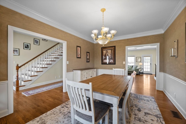 dining space featuring stairs, a chandelier, wood finished floors, and wainscoting