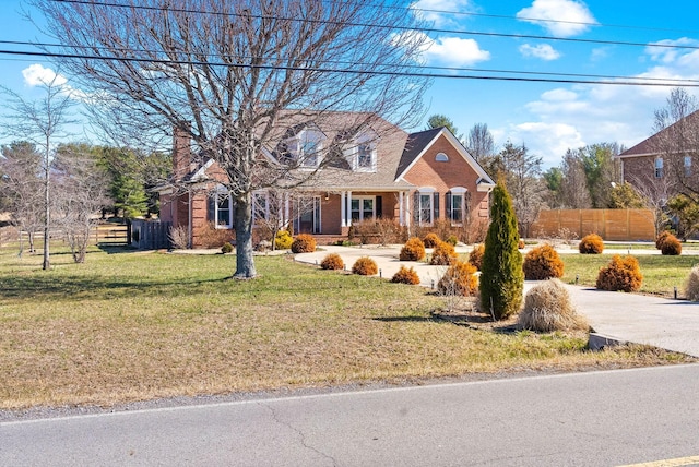 cape cod-style house featuring a front yard, fence, driveway, a chimney, and brick siding