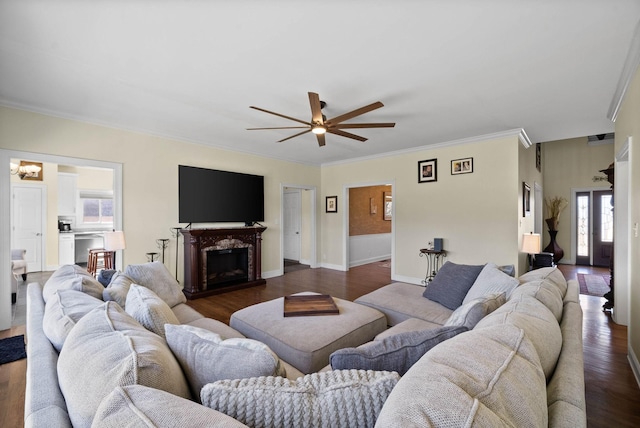 living area featuring a ceiling fan, dark wood finished floors, a fireplace, crown molding, and baseboards