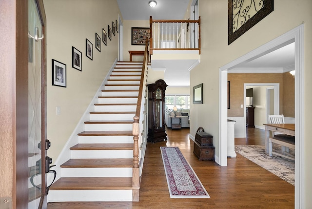 entryway with wood finished floors, crown molding, baseboards, a towering ceiling, and stairs