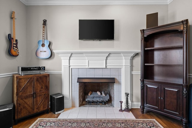 living room with wood finished floors, a tiled fireplace, and ornamental molding