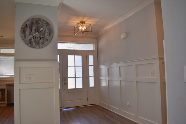 entryway with dark wood-style floors, an inviting chandelier, ornamental molding, wainscoting, and a decorative wall