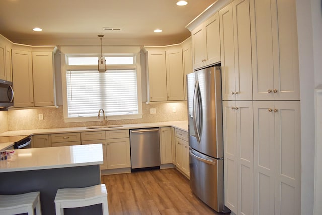 kitchen with light wood finished floors, a sink, stainless steel appliances, light countertops, and a kitchen bar