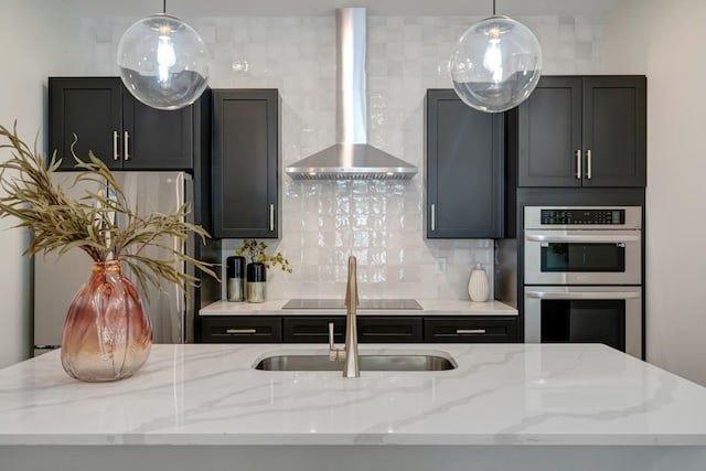 kitchen featuring backsplash, wall chimney range hood, pendant lighting, stainless steel appliances, and a sink