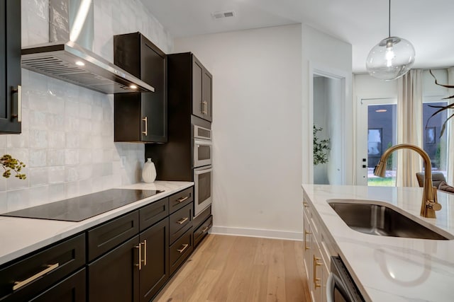 kitchen with visible vents, wall chimney range hood, light wood-style flooring, black electric cooktop, and a sink