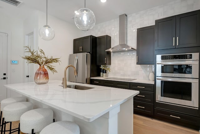 kitchen with visible vents, light wood-style flooring, a kitchen breakfast bar, stainless steel appliances, and wall chimney range hood