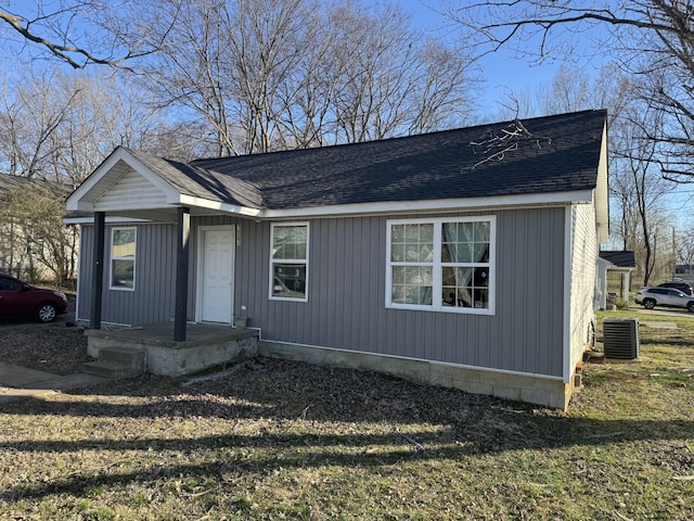 view of front facade with a front lawn, cooling unit, and a shingled roof