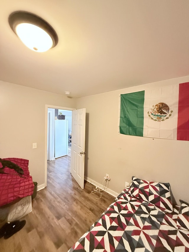 bedroom featuring baseboards, wood finished floors, and freestanding refrigerator