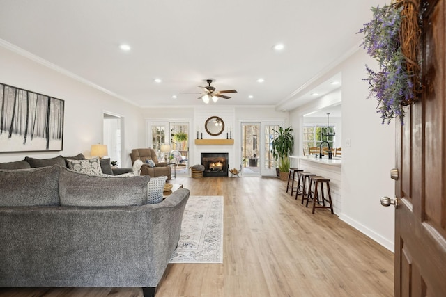 living area with baseboards, light wood-style flooring, a lit fireplace, ceiling fan, and crown molding