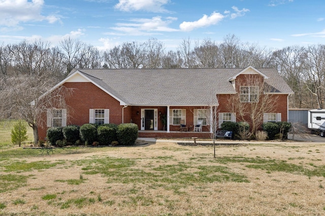 view of front of property featuring brick siding, covered porch, a front lawn, and roof with shingles