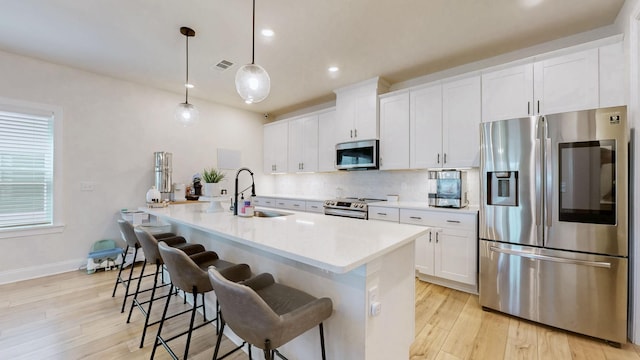 kitchen featuring visible vents, a center island with sink, a sink, stainless steel appliances, and tasteful backsplash