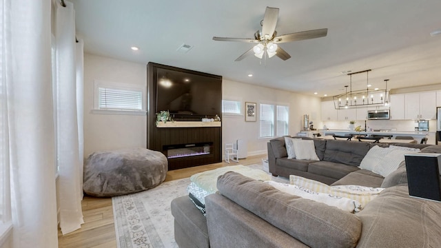 living area featuring light wood finished floors, visible vents, recessed lighting, and ceiling fan with notable chandelier