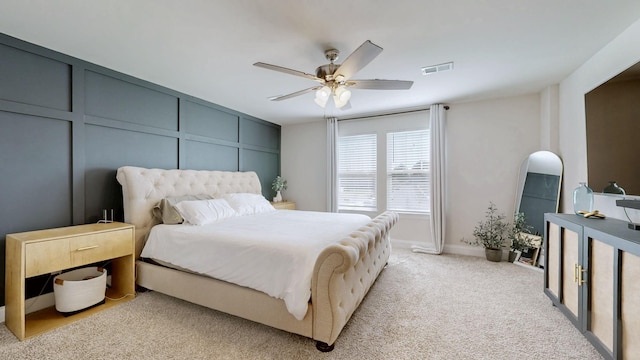 bedroom featuring visible vents, light carpet, arched walkways, a decorative wall, and ceiling fan