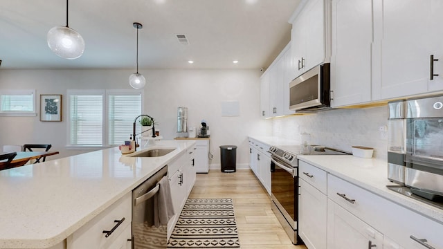 kitchen with backsplash, decorative light fixtures, appliances with stainless steel finishes, white cabinets, and a sink