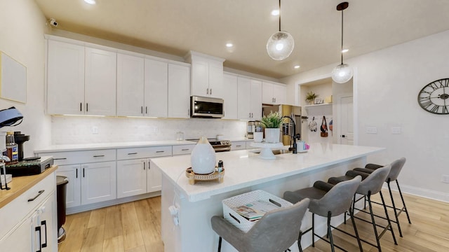 kitchen with light wood finished floors, tasteful backsplash, a breakfast bar area, white cabinets, and stainless steel appliances