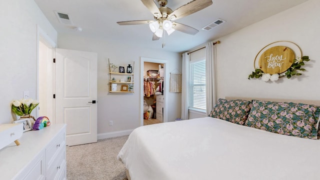 bedroom featuring visible vents, light carpet, baseboards, and a walk in closet