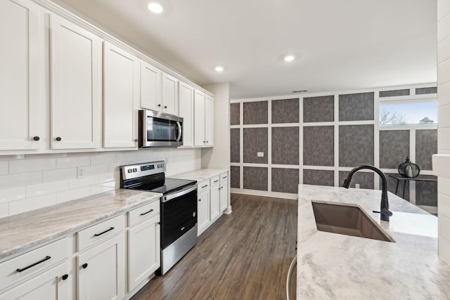 kitchen with dark wood finished floors, decorative backsplash, appliances with stainless steel finishes, white cabinetry, and a sink