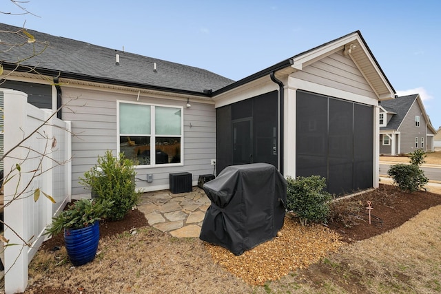 rear view of property featuring a patio, a garage, a sunroom, and roof with shingles