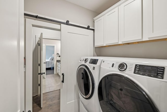 washroom with wood finished floors, washing machine and dryer, a barn door, and cabinet space