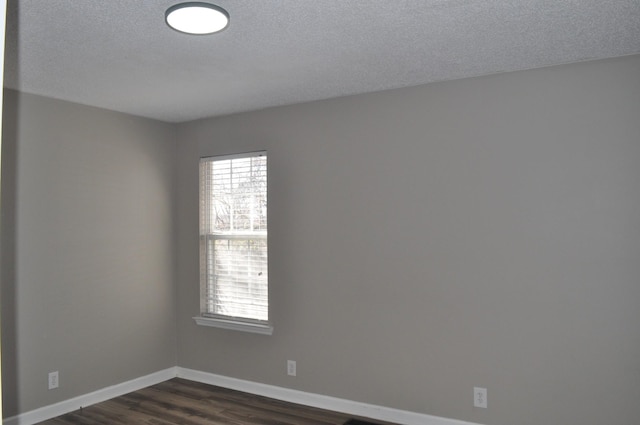 empty room featuring dark wood-type flooring, baseboards, and a textured ceiling