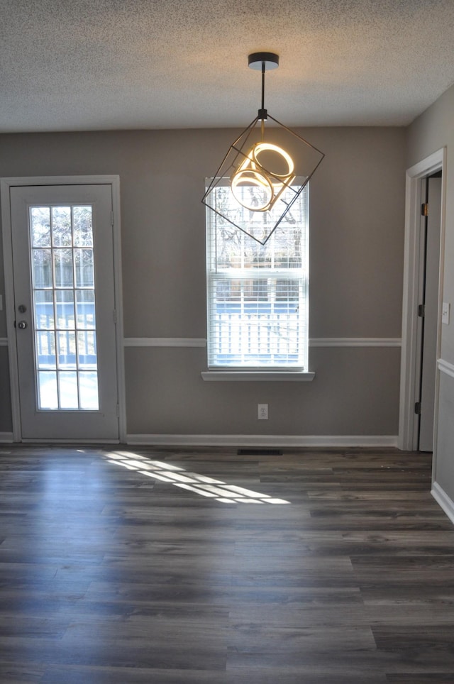 unfurnished dining area featuring a textured ceiling, baseboards, and wood finished floors