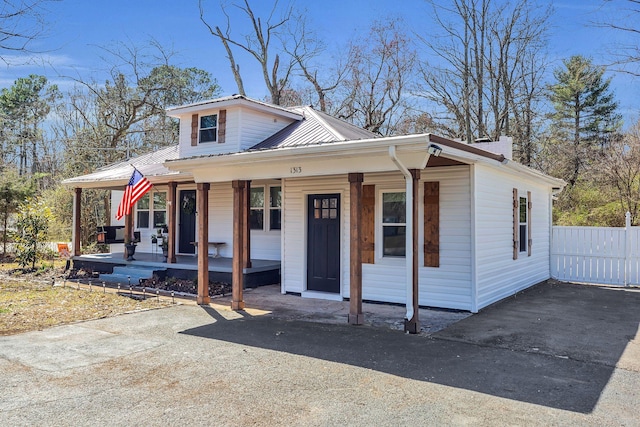 bungalow featuring covered porch, metal roof, and fence