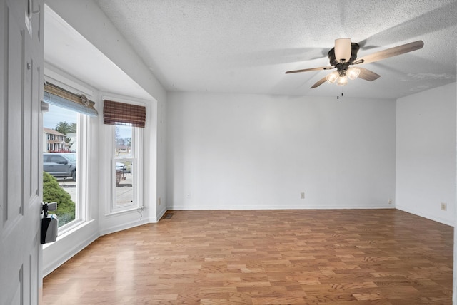 spare room featuring baseboards, a textured ceiling, light wood-style flooring, and a ceiling fan