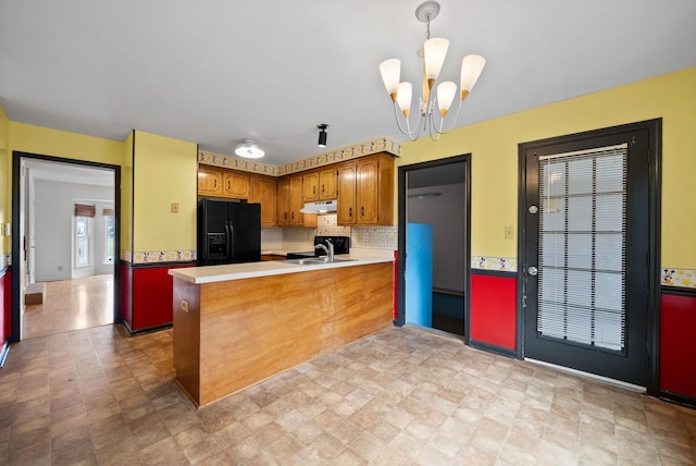 kitchen with black fridge, under cabinet range hood, a sink, a peninsula, and light countertops