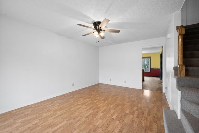 empty room with ceiling fan, stairway, light wood finished floors, and a textured ceiling