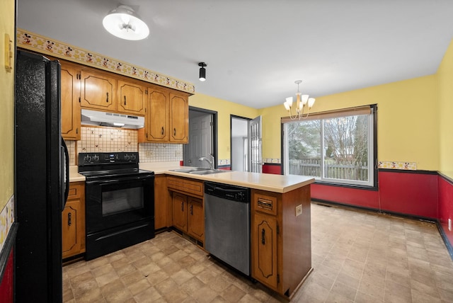 kitchen with brown cabinetry, a peninsula, a sink, black appliances, and under cabinet range hood