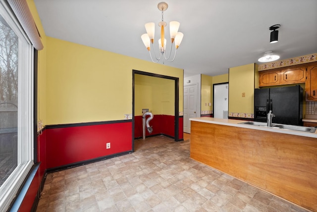 kitchen with light countertops, a peninsula, brown cabinetry, black fridge with ice dispenser, and a sink