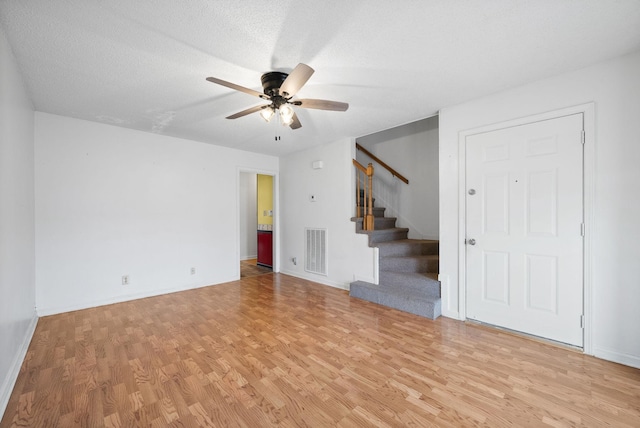 unfurnished living room with visible vents, ceiling fan, stairs, light wood-style floors, and a textured ceiling