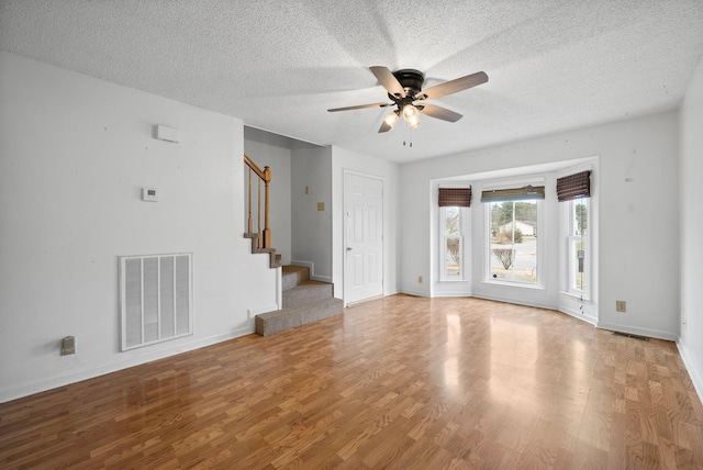 unfurnished living room featuring stairs, wood finished floors, visible vents, and a textured ceiling