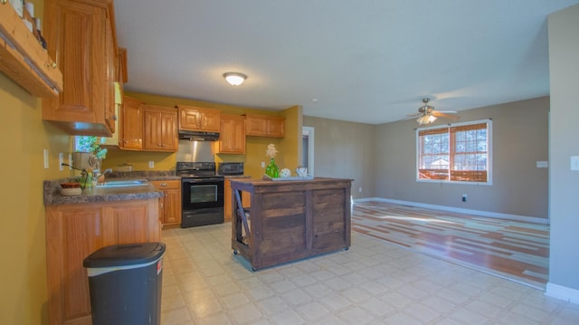 kitchen featuring dark countertops, under cabinet range hood, light floors, black appliances, and a sink