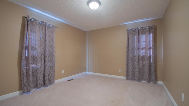 spare room featuring baseboards, visible vents, carpet floors, and a textured ceiling