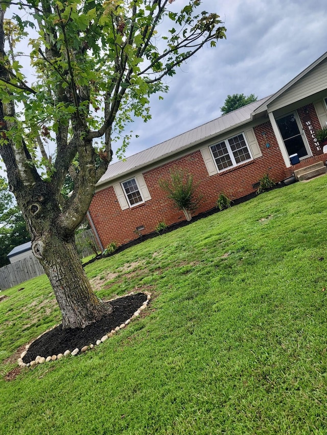 view of side of home featuring a yard, brick siding, metal roof, and fence