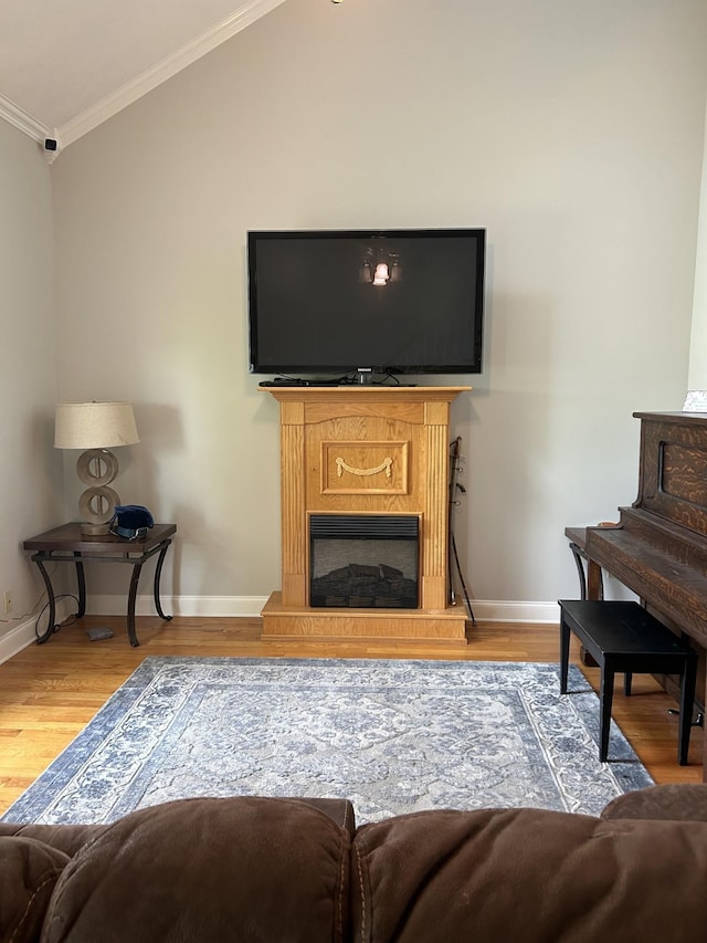 living area with ornamental molding, wood finished floors, a fireplace, baseboards, and vaulted ceiling