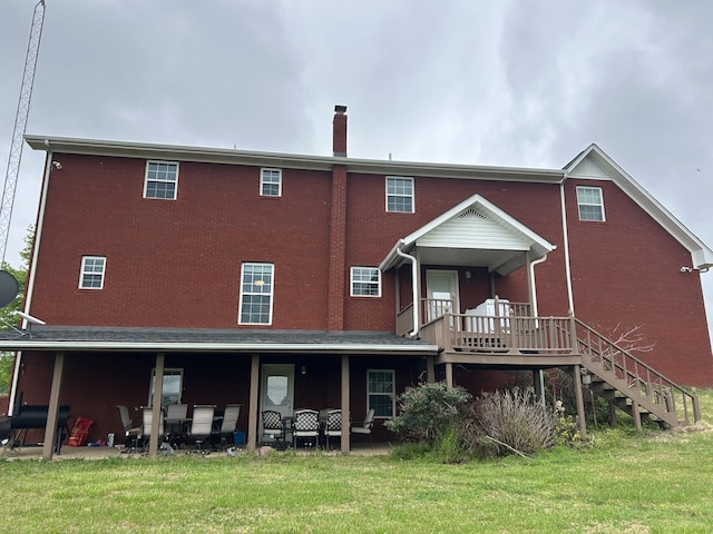 rear view of property with stairway, a yard, brick siding, and a chimney