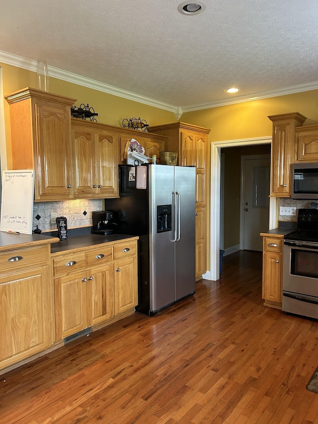 kitchen featuring dark wood-style flooring, ornamental molding, stainless steel appliances, dark countertops, and tasteful backsplash