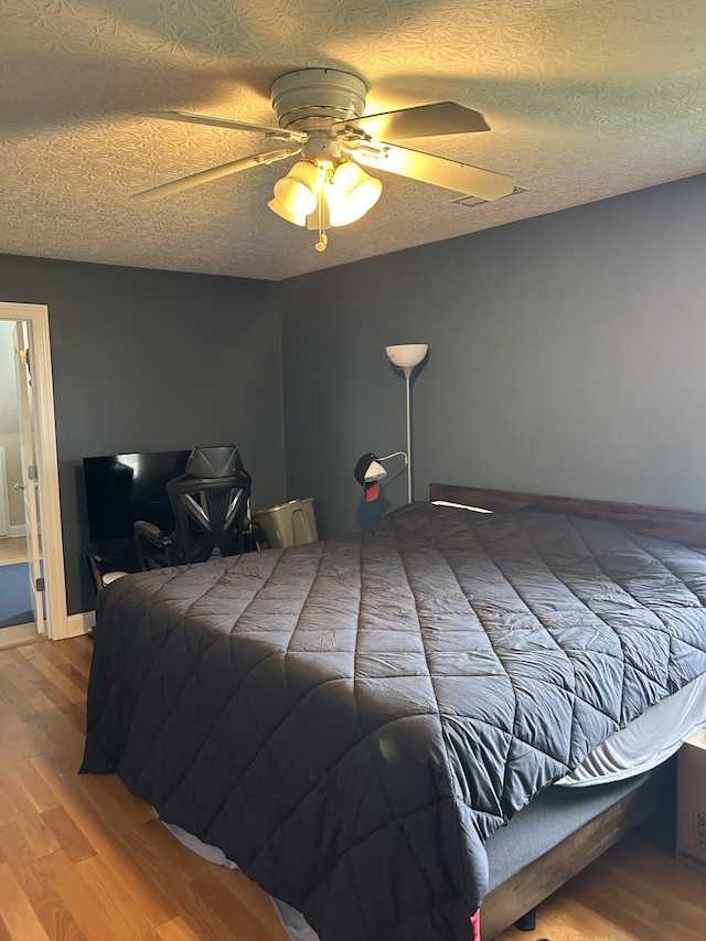 bedroom with baseboards, a textured ceiling, a ceiling fan, and wood finished floors