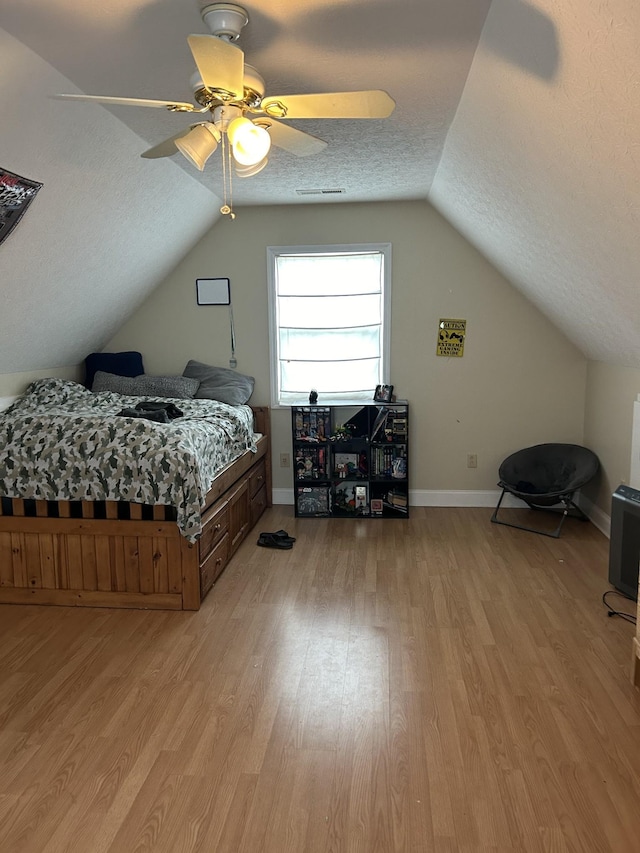 bedroom with baseboards, a textured ceiling, light wood-style floors, and vaulted ceiling