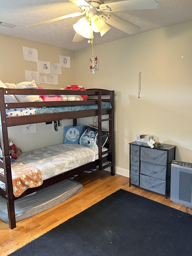 bedroom featuring wood finished floors, baseboards, visible vents, ceiling fan, and a textured ceiling