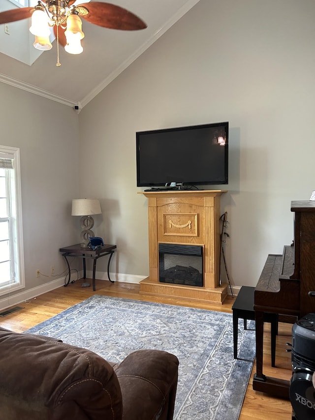 living room featuring crown molding, baseboards, vaulted ceiling, light wood-style floors, and a glass covered fireplace