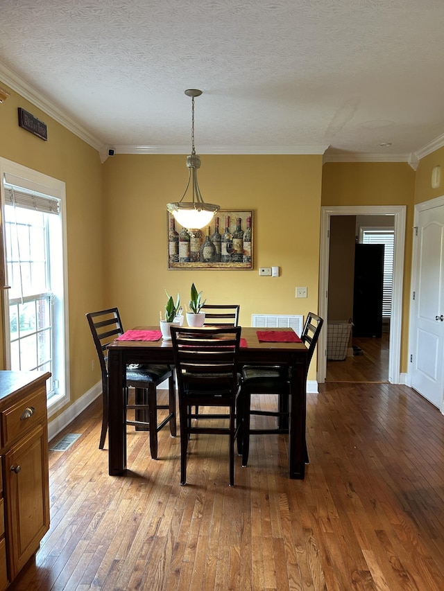 dining space with visible vents, ornamental molding, a textured ceiling, light wood finished floors, and baseboards