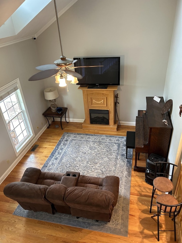 living area with a glass covered fireplace, wood finished floors, baseboards, and high vaulted ceiling