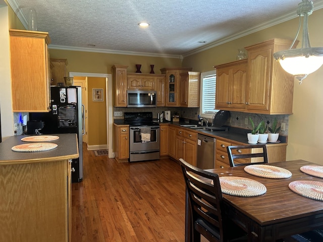 kitchen featuring stainless steel appliances, dark countertops, wood finished floors, and crown molding