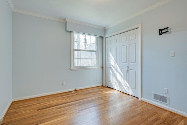 unfurnished bedroom with hardwood / wood-style floors, baseboards, visible vents, ornamental molding, and a closet