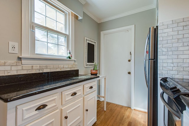 kitchen with light wood finished floors, dark stone counters, ornamental molding, freestanding refrigerator, and white cabinetry