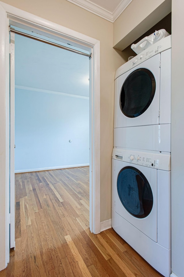 clothes washing area with stacked washer and dryer, ornamental molding, wood finished floors, baseboards, and laundry area