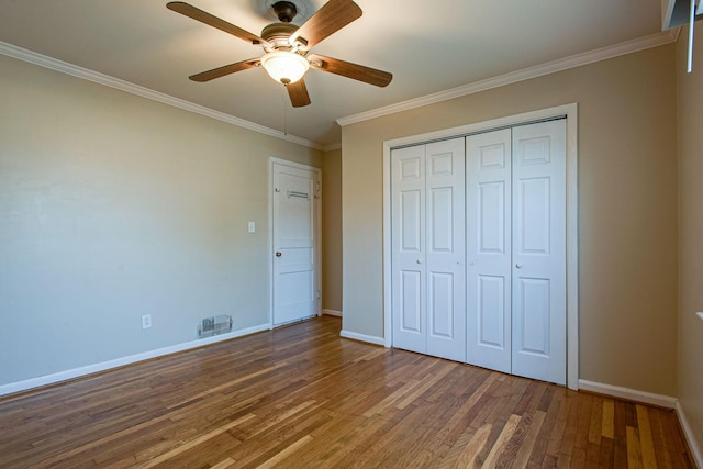 unfurnished bedroom featuring visible vents, baseboards, ornamental molding, wood finished floors, and a closet